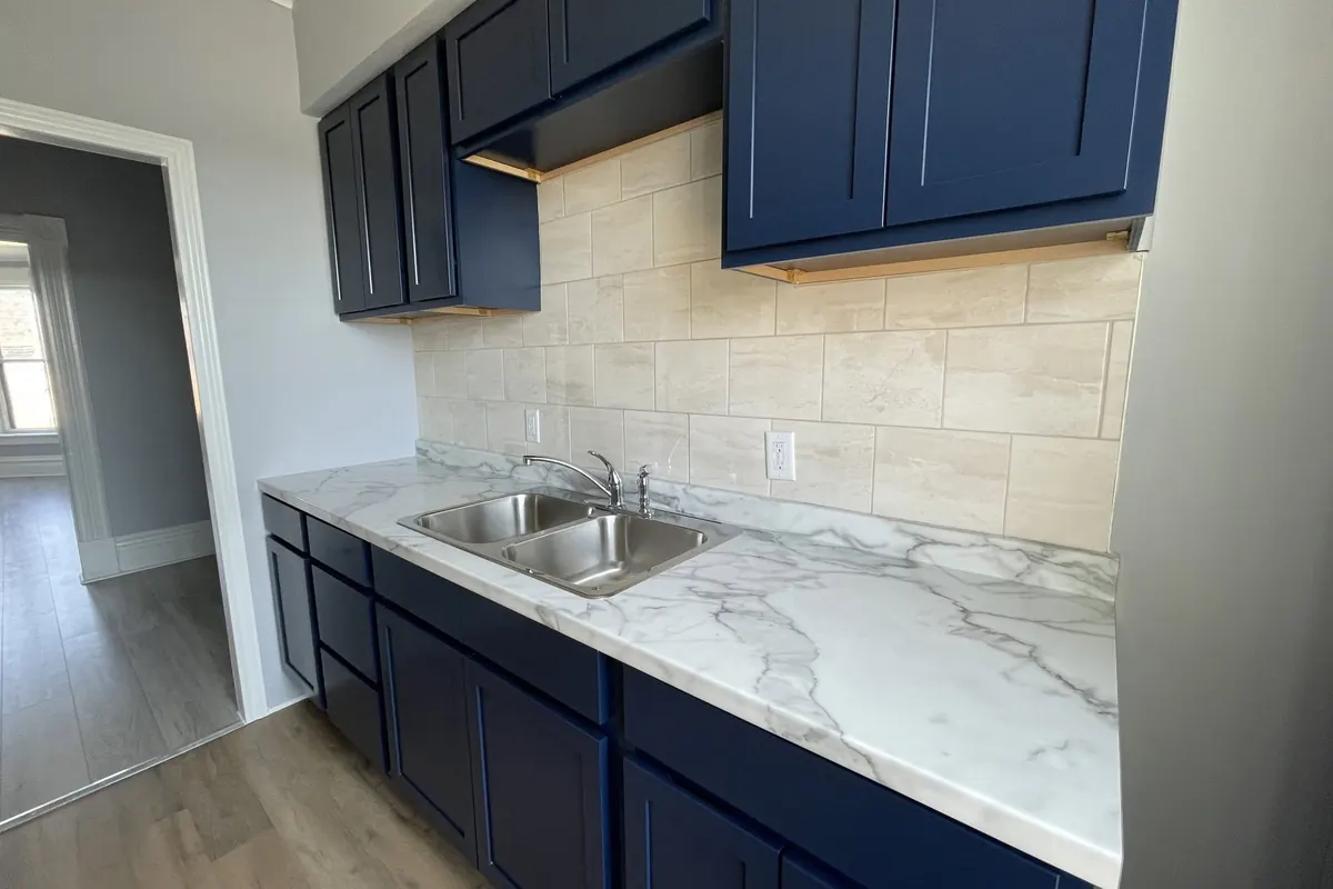 A kitchen with navy shaker cabinets, marble-look counters, a double sink and a large-tile backsplash.