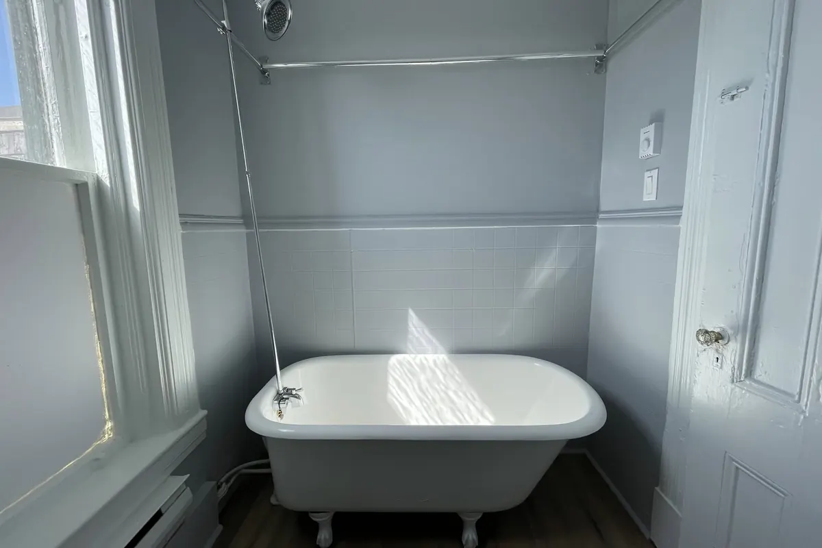 A bathroom with a white clawfoot tub under a tall window and grey walls.
