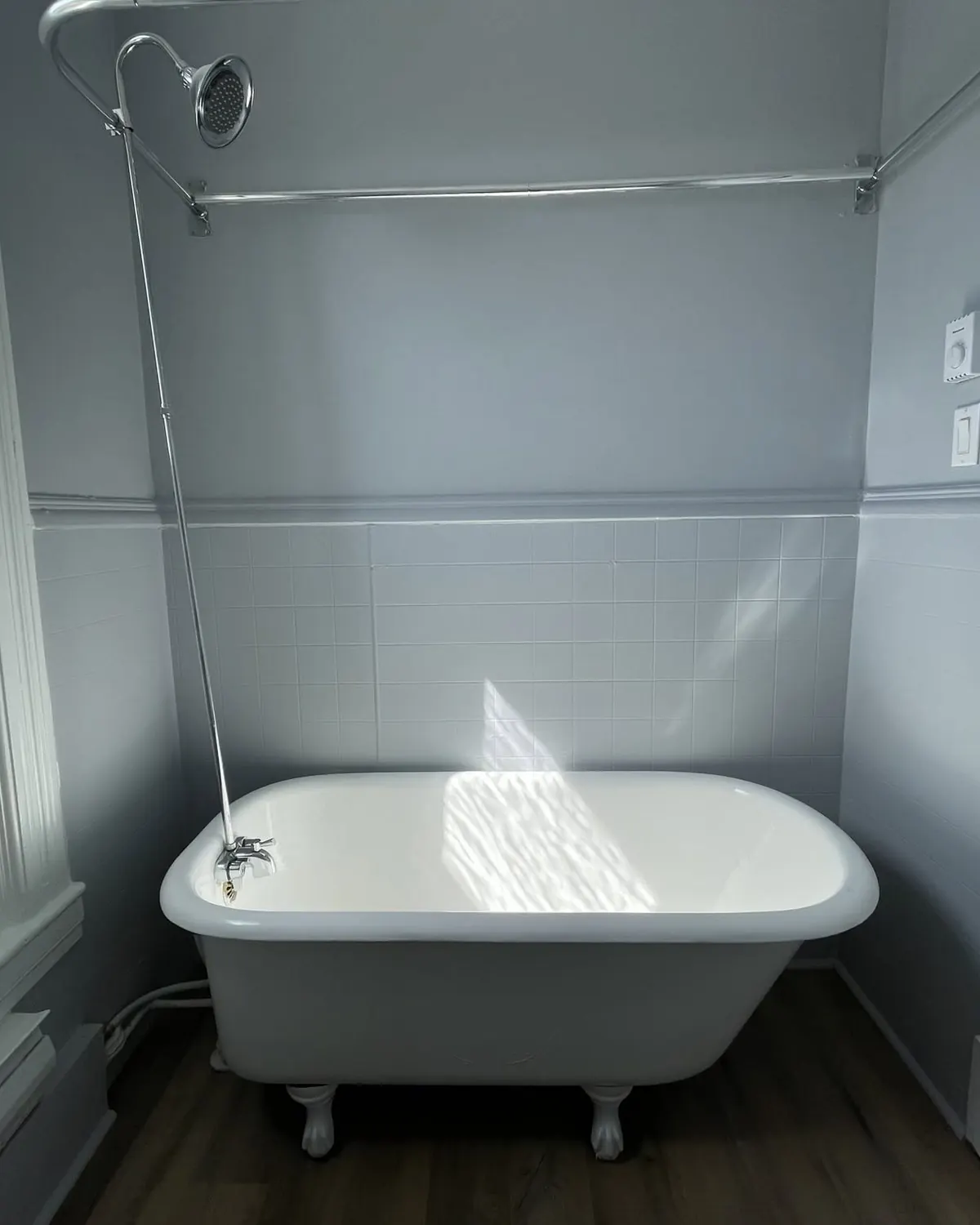 A bathroom with a white clawfoot tub under a tall window and grey walls.