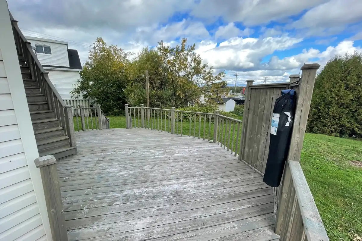 A wide wooden back deck with railings and stairs, a lawn and trees behind.