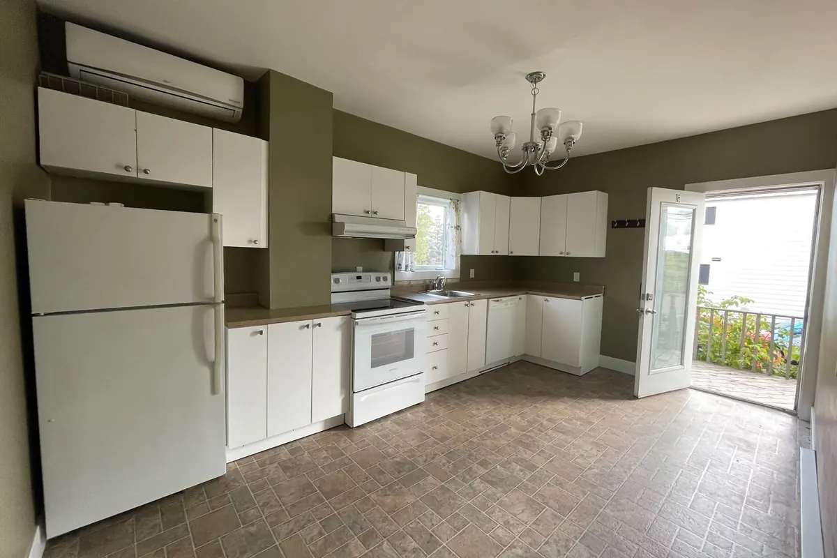 A kitchen with white cabinets and appliances, a chandelier and a glass door out to a deck.