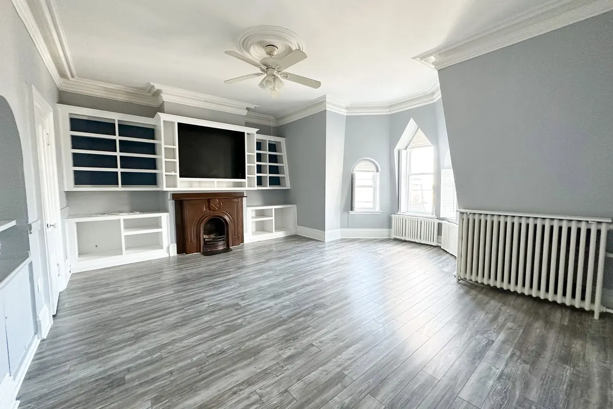 The same room finished: white built-in shelves around a brick fireplace, grey plank floors, a ceiling fan and arched windows.