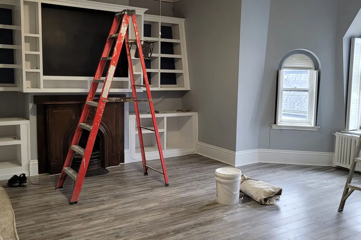 The same room mid-job: built-in shelves around the fireplace, a ladder, paint pails and floor going down.