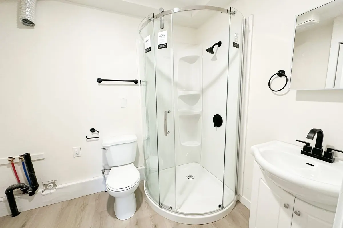 A bathroom with a curved glass corner shower, a white vanity with a black faucet and a toilet.