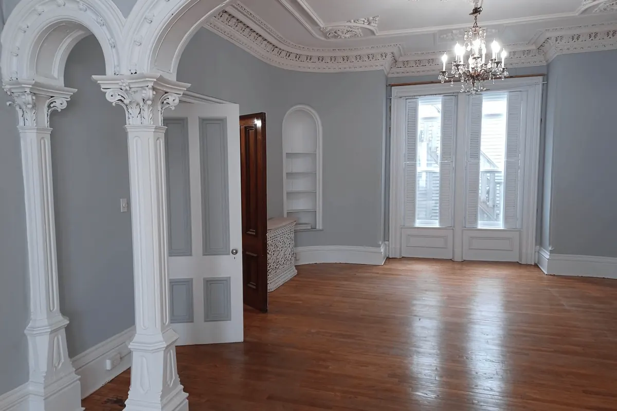 A restored room: white columns and arches, a plaster ceiling with a chandelier, and wood floors.